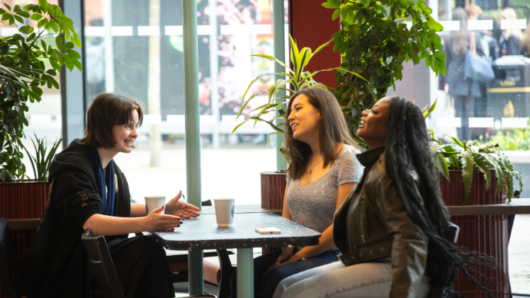 three female students sat around a table chatting